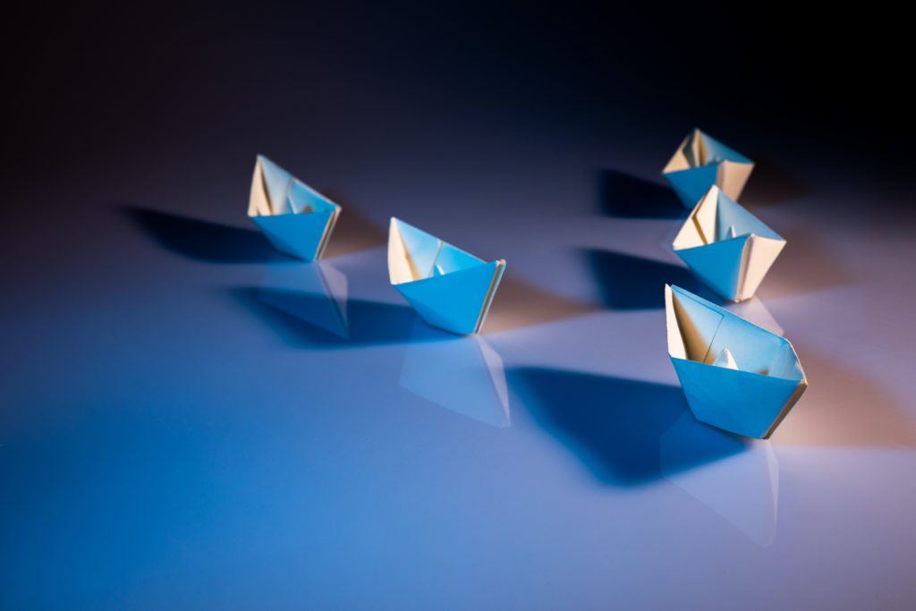 one paper boat leading four other paper boats