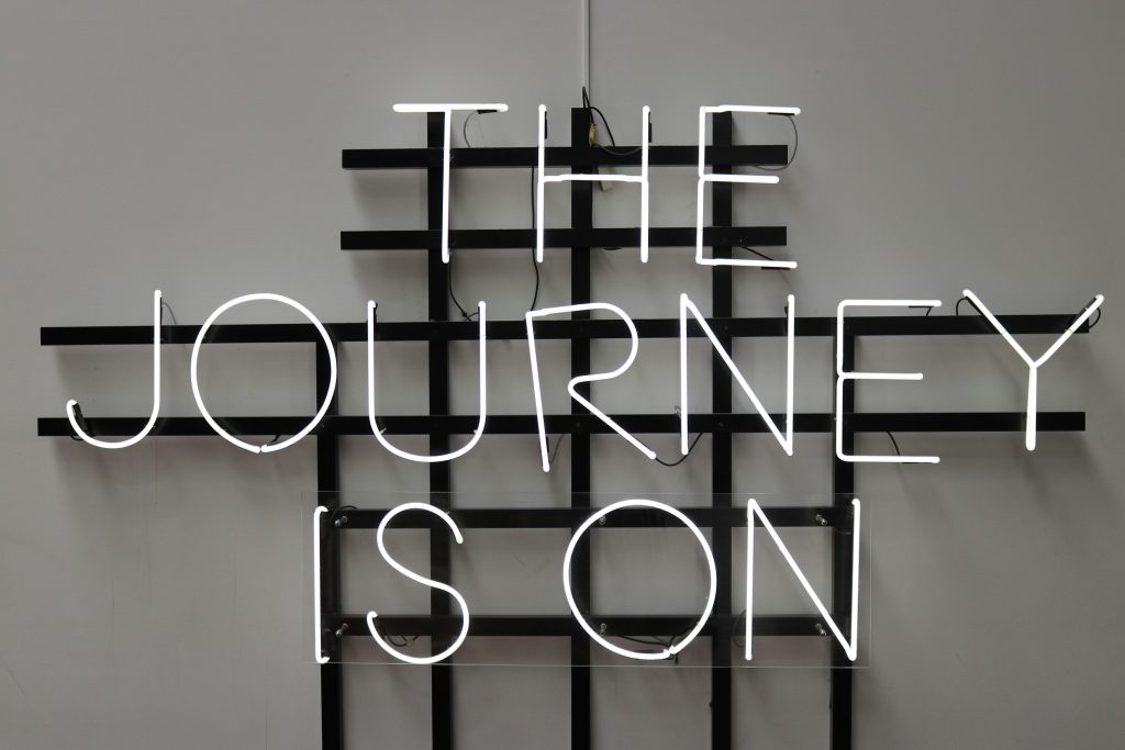 An unlit neon sign that reads "The Journey Is On" in all capital letters.