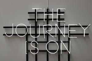 An unlit neon sign that reads "The Journey Is On" in all capital letters.