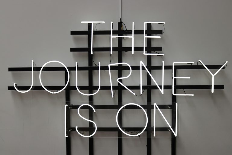 An unlit neon sign that reads "The Journey Is On" in all capital letters.