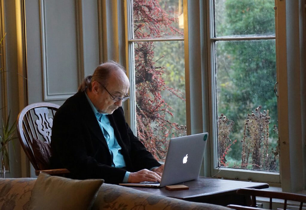 An elderly man sits and uses a computer.
