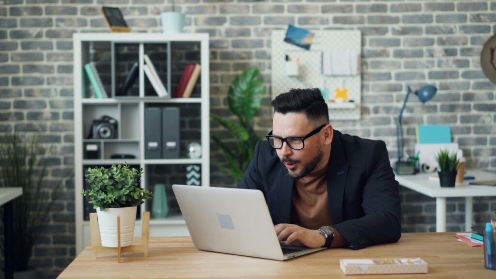 A young man uses a MacBook while sitting at a table.