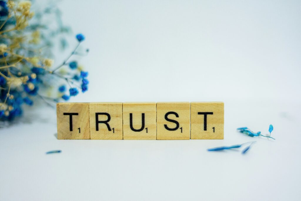 The word "TRUST" is spelled out with Scrabble letters in front of a background with flowers.