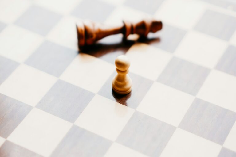 A small white pawn stands upright on a chessboard while a larger fallen king lies defeated in the background, illustrating how a smaller, more focused competitor can outperform a larger one.