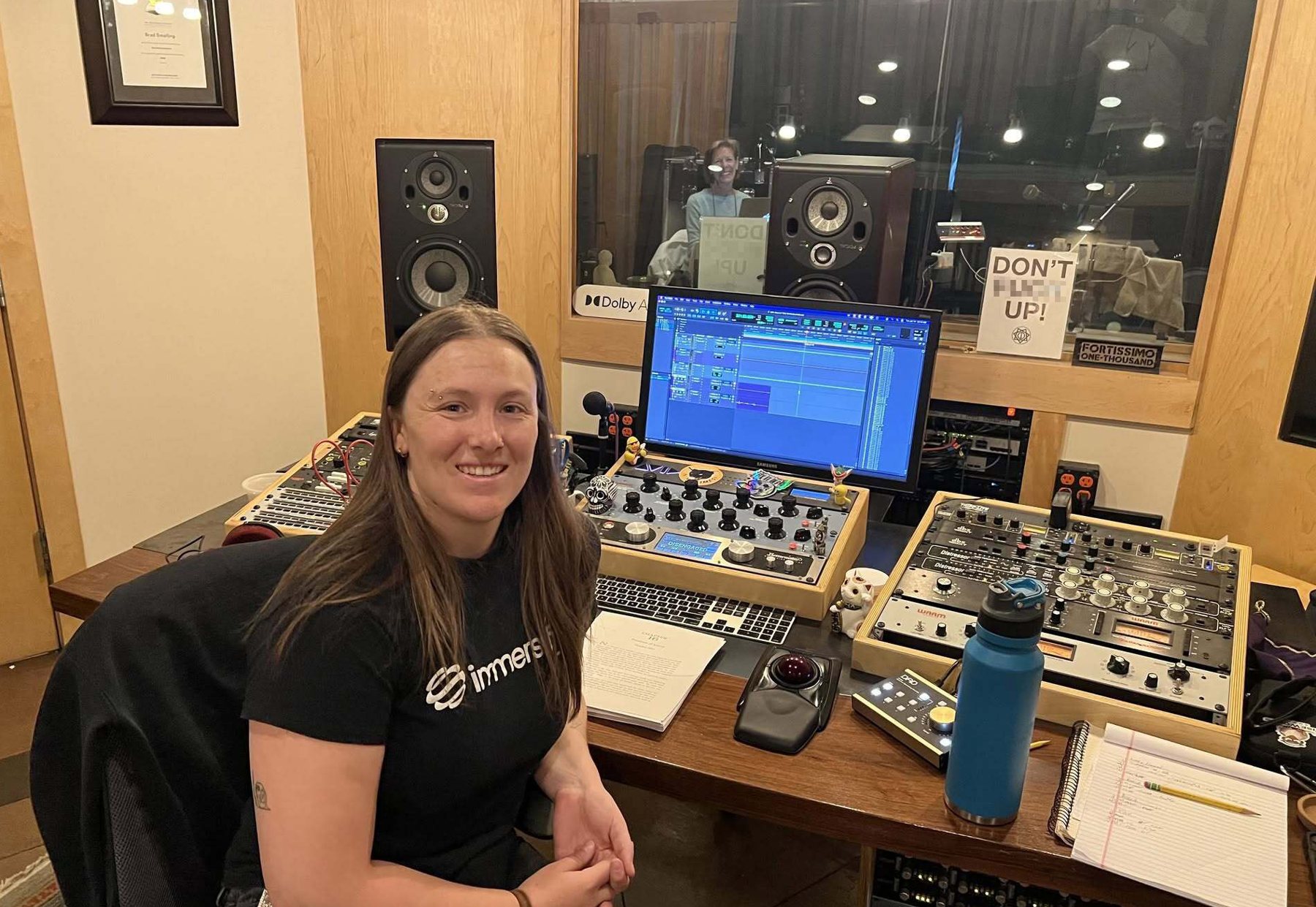 An audio engineer at the mixing console at Evergroove Studio, with a narrator visible through the control-room window