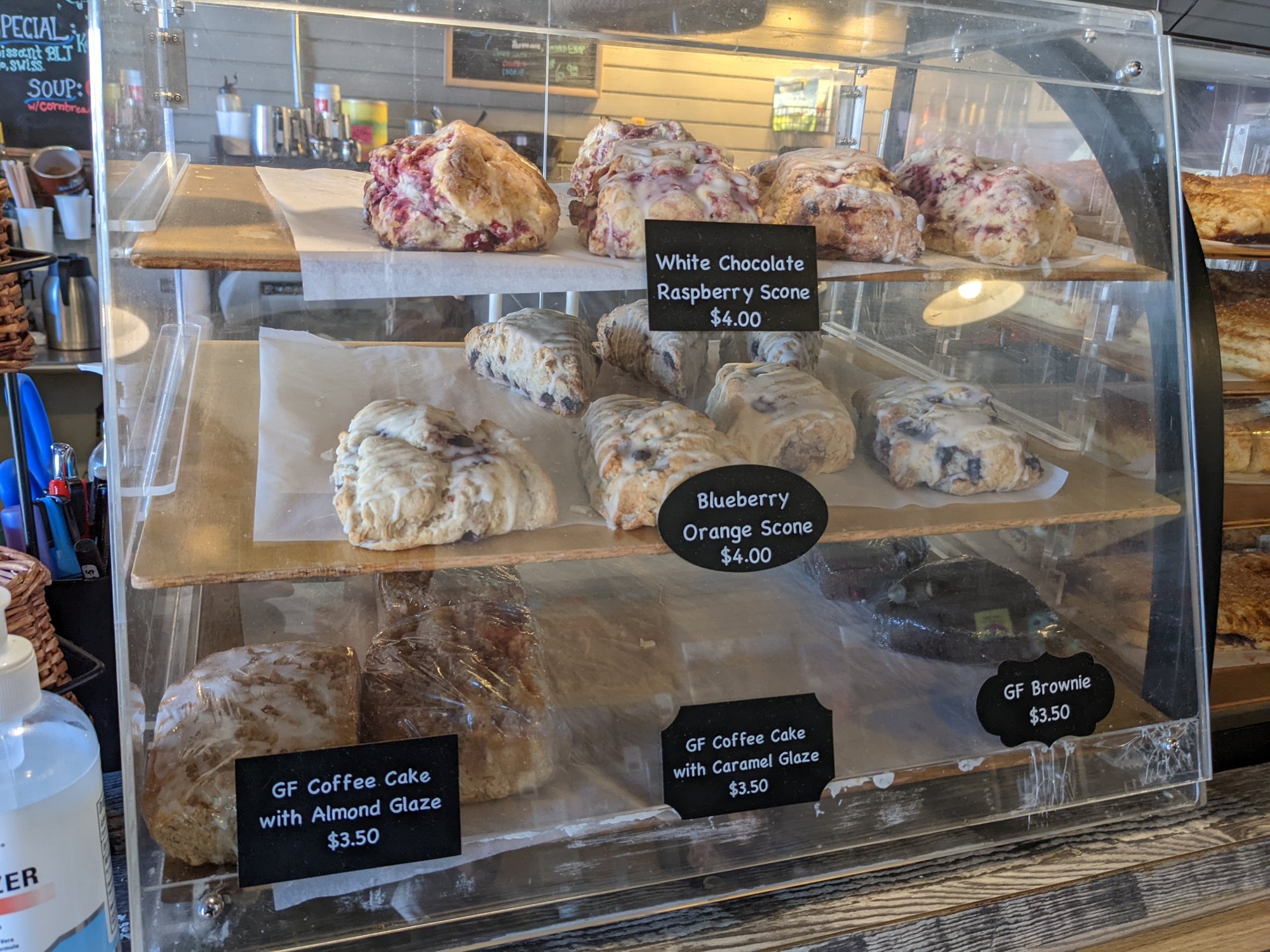 A bakery case of raspberry and blueberry scones and coffee cake with chalkboard price tags
