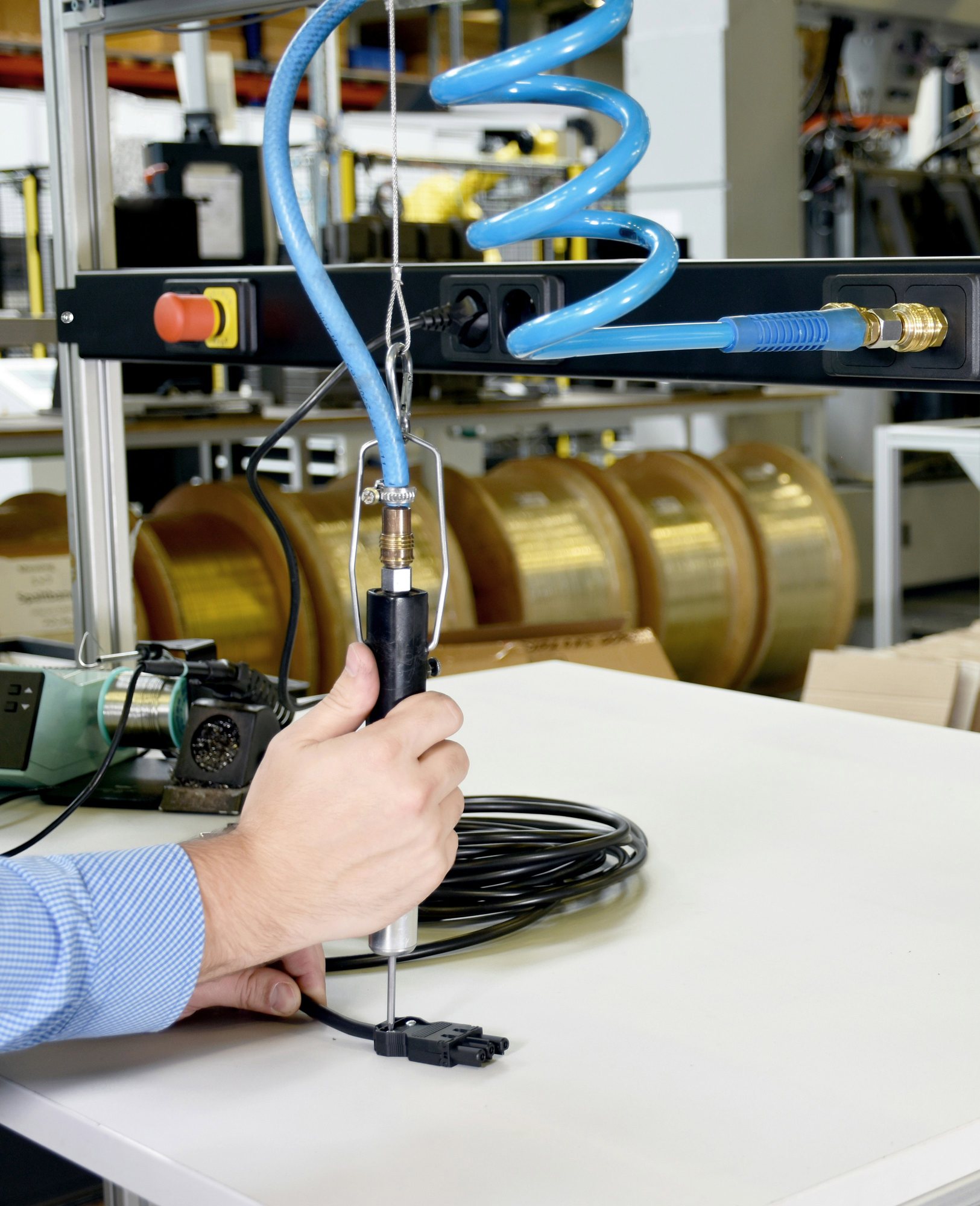 A hand testing a cable assembly with a tool hanging from a workbench rig in a manufacturing shop