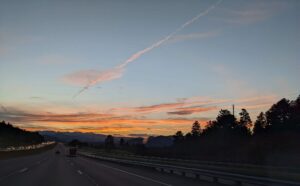 An orange and pink sunset over dark mountain silhouettes, seen from the westbound lanes of I-70