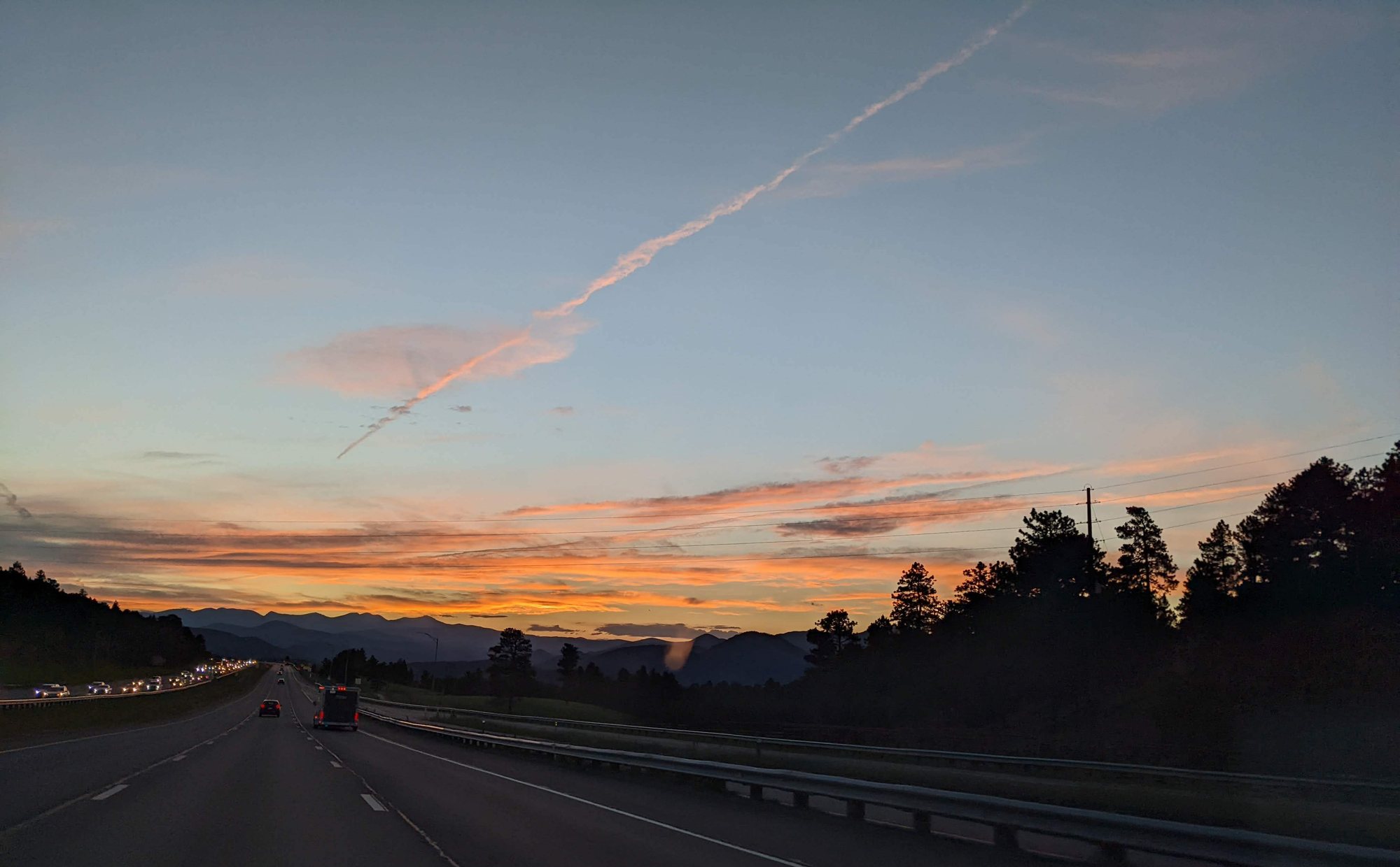 An orange and pink sunset over dark mountain silhouettes, seen from the westbound lanes of I-70