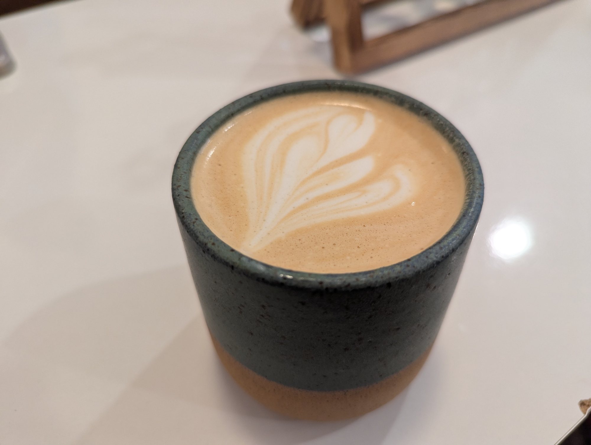 A latte with leaf-shaped foam art in a dark stoneware cup on a white table