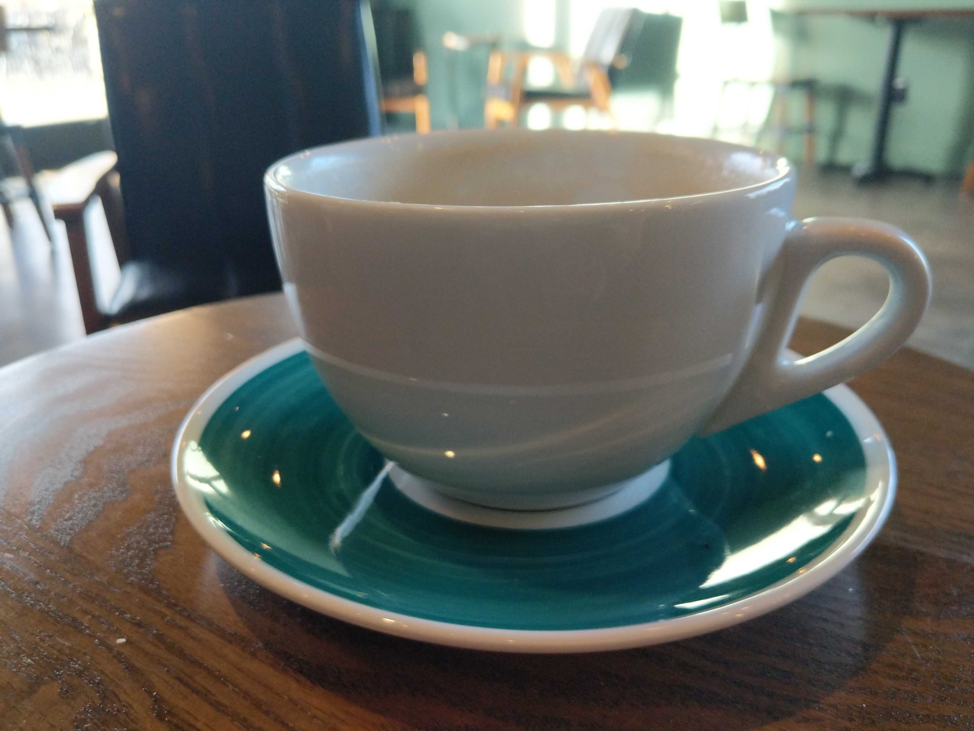 A white cup on a teal saucer on a wooden cafe table