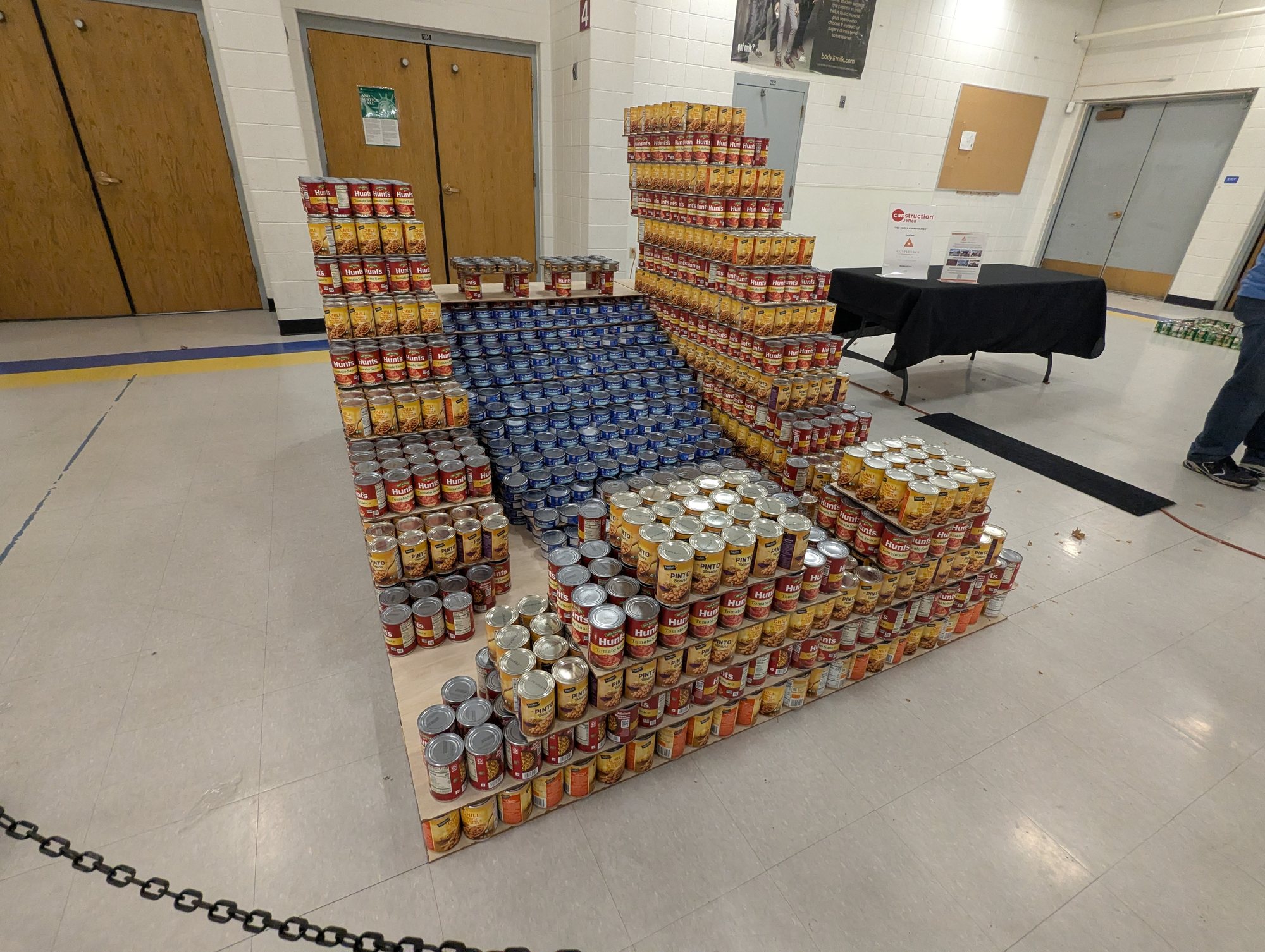 A sculpture of a chair built from hundreds of stacked food cans, on a gym floor