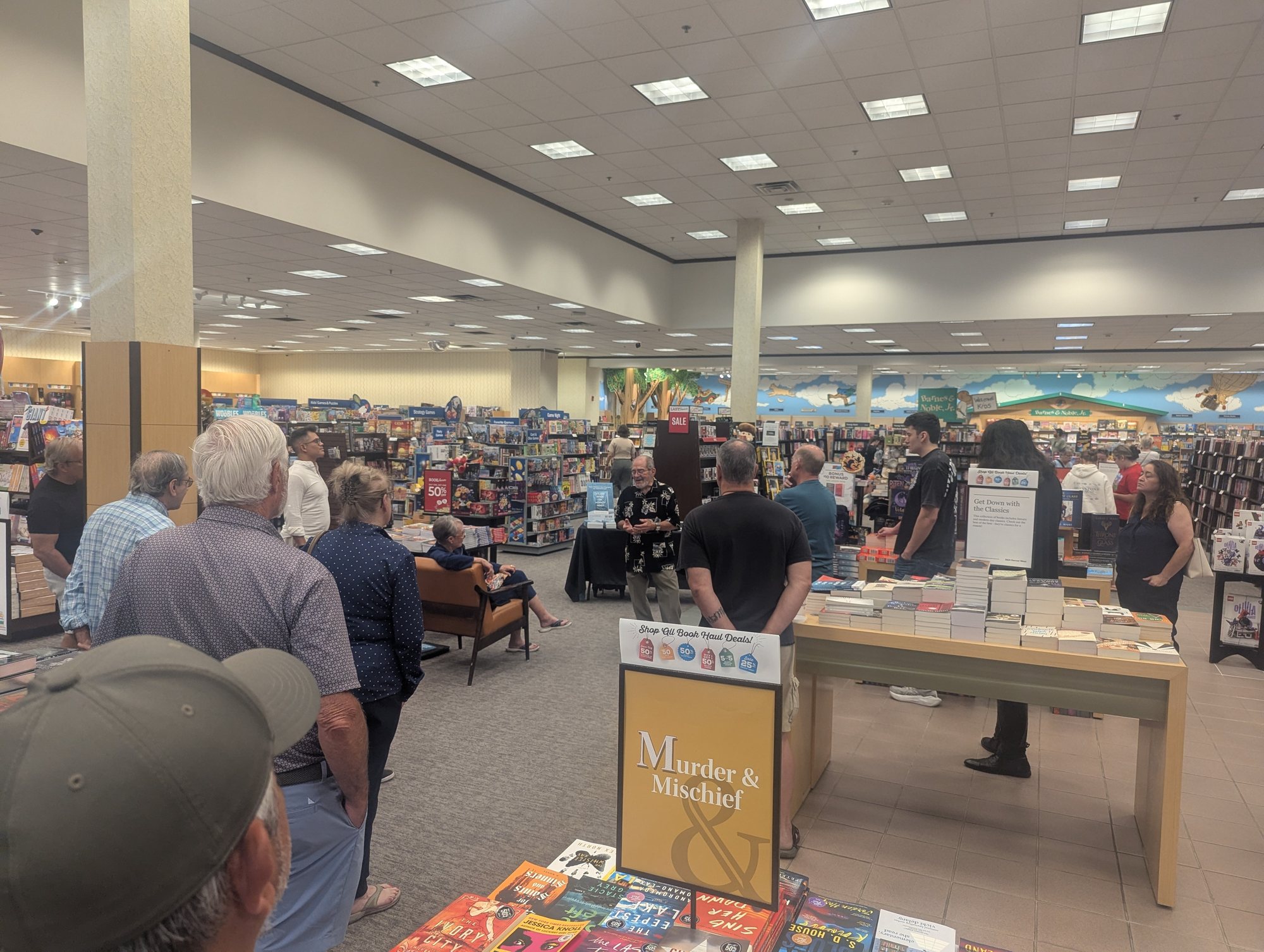 Shoppers gathered among the bookshelves of a Barnes & Noble, listening to an author speak