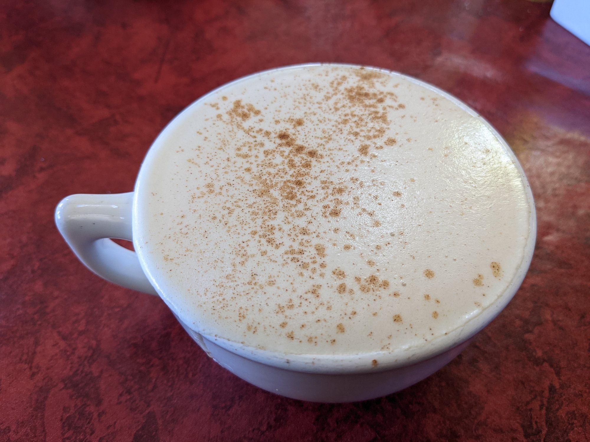 A white cup of latte with cinnamon on top, on a red table