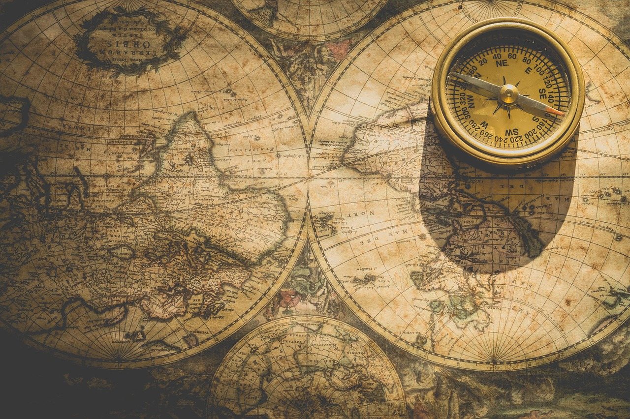 A brass compass resting on an antique map of the world drawn as two hemispheres, in warm sepia tones